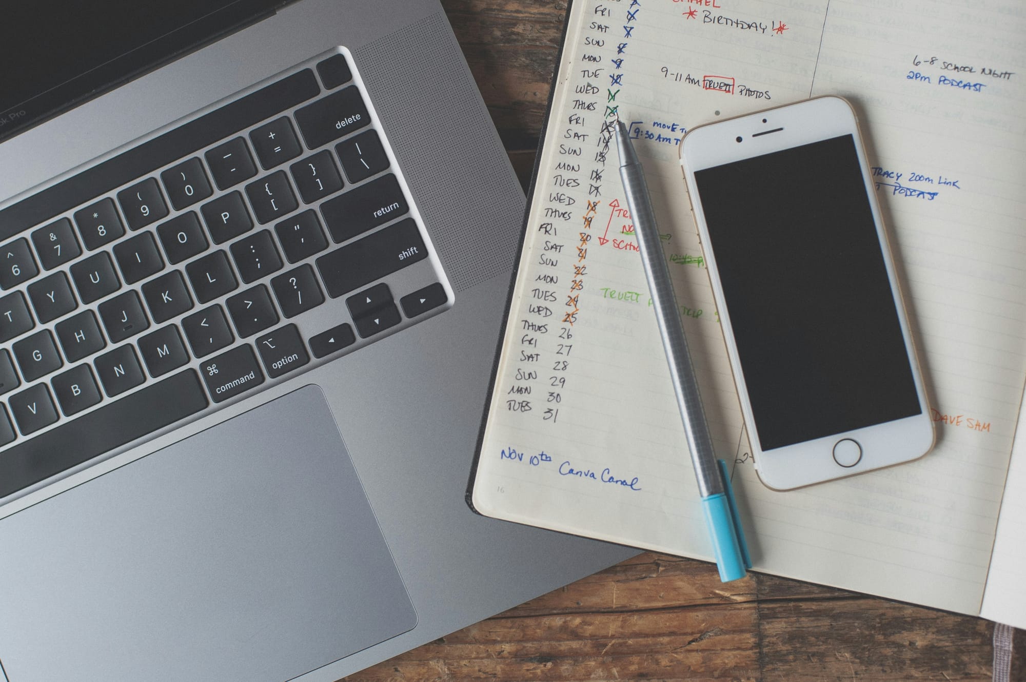 A laptop, an open notebook, an iPhone, and a pen are on the desk