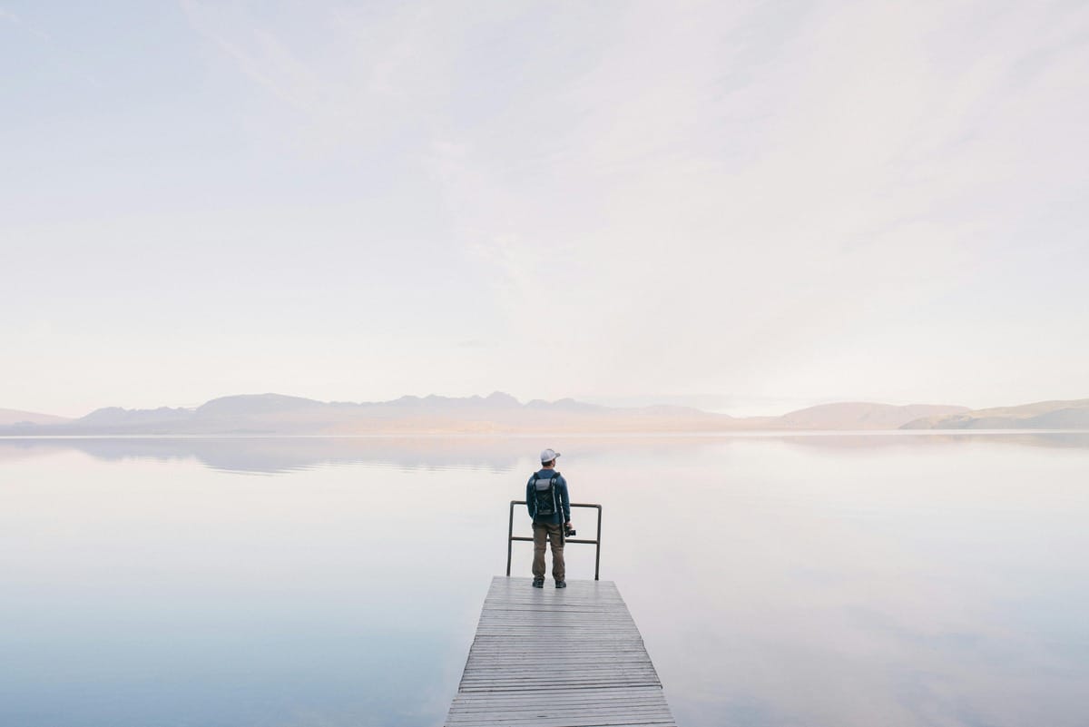 Photographer Wearing Jacket Standing on Wooden Docks Leading to Body of Water